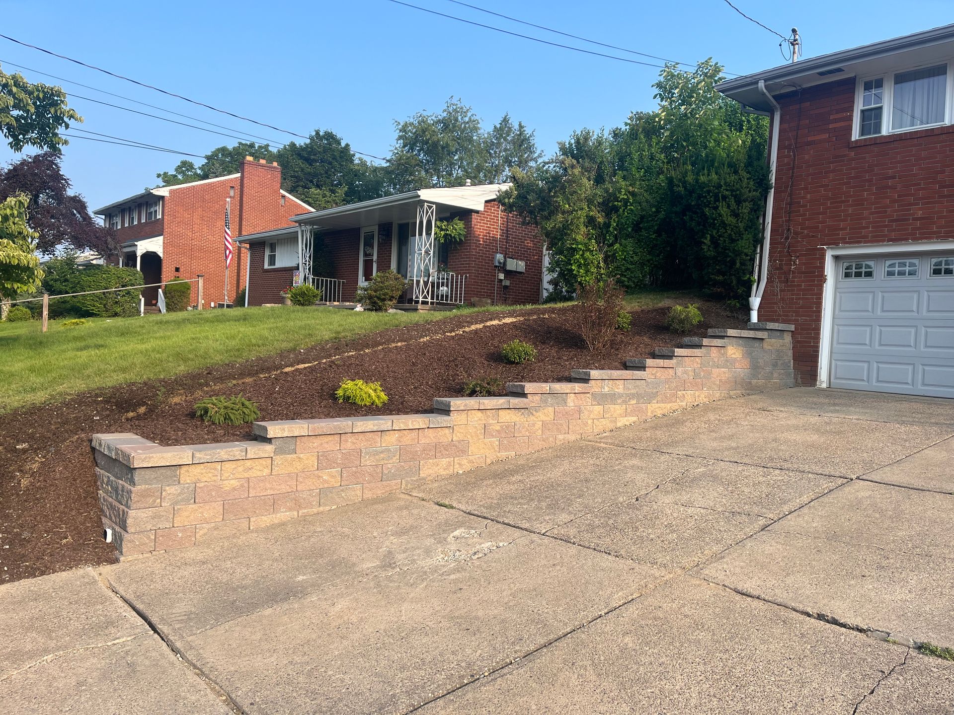 A brick house is sitting on top of a hill next to a garage.