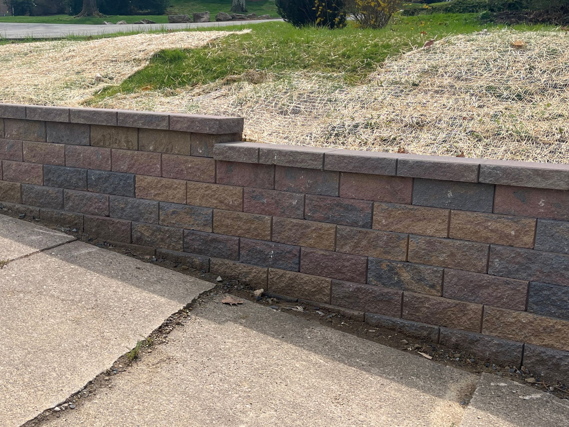 A brick wall along a sidewalk next to a grassy field.