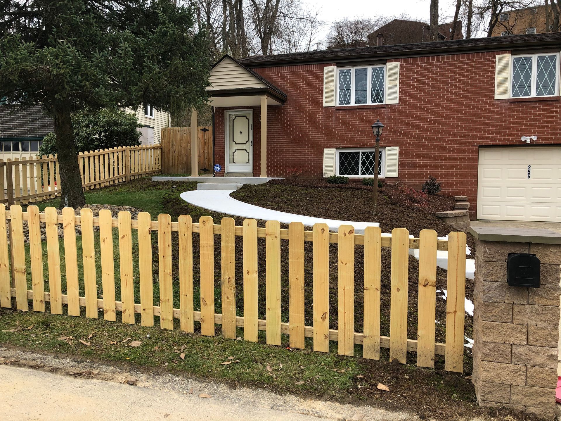 A wooden picket fence is in front of a brick house.
