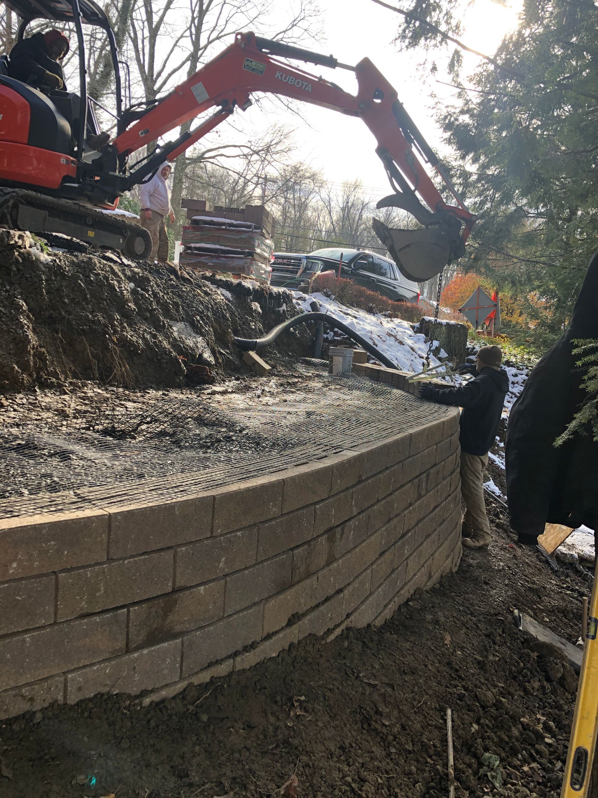 An excavator is digging a hole in the ground next to a brick wall.