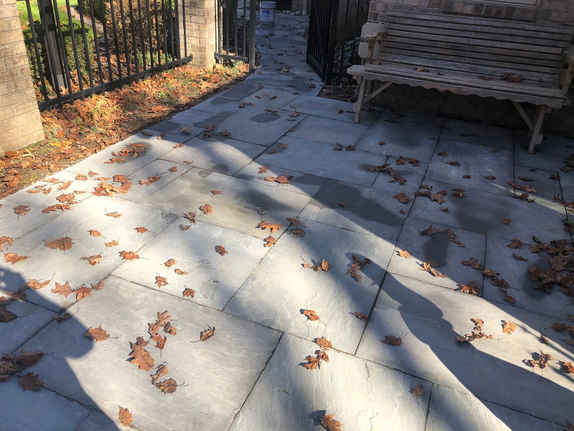 A patio with leaves on it and a bench in the background.