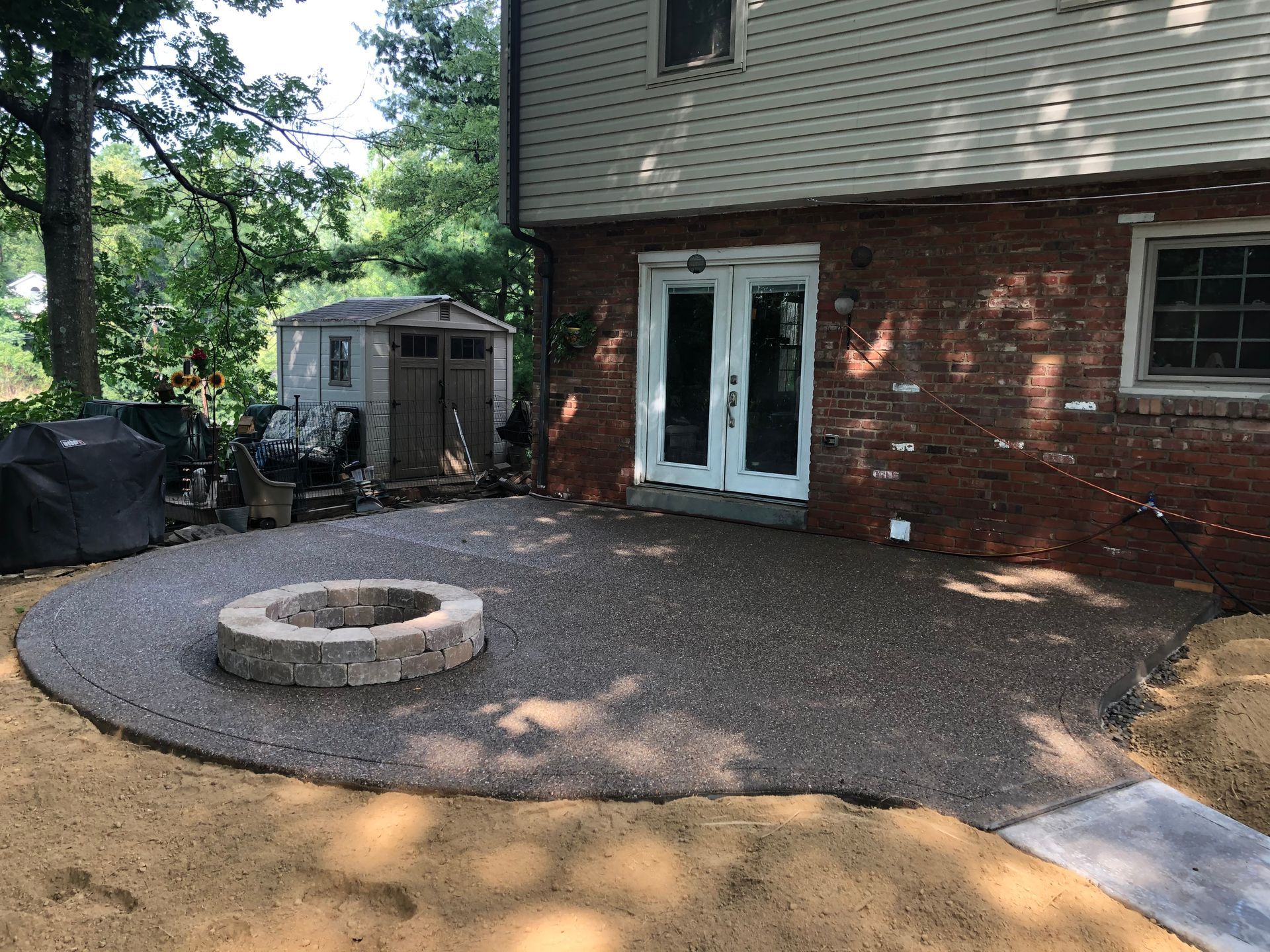 A fire pit is in the middle of a patio in front of a house.