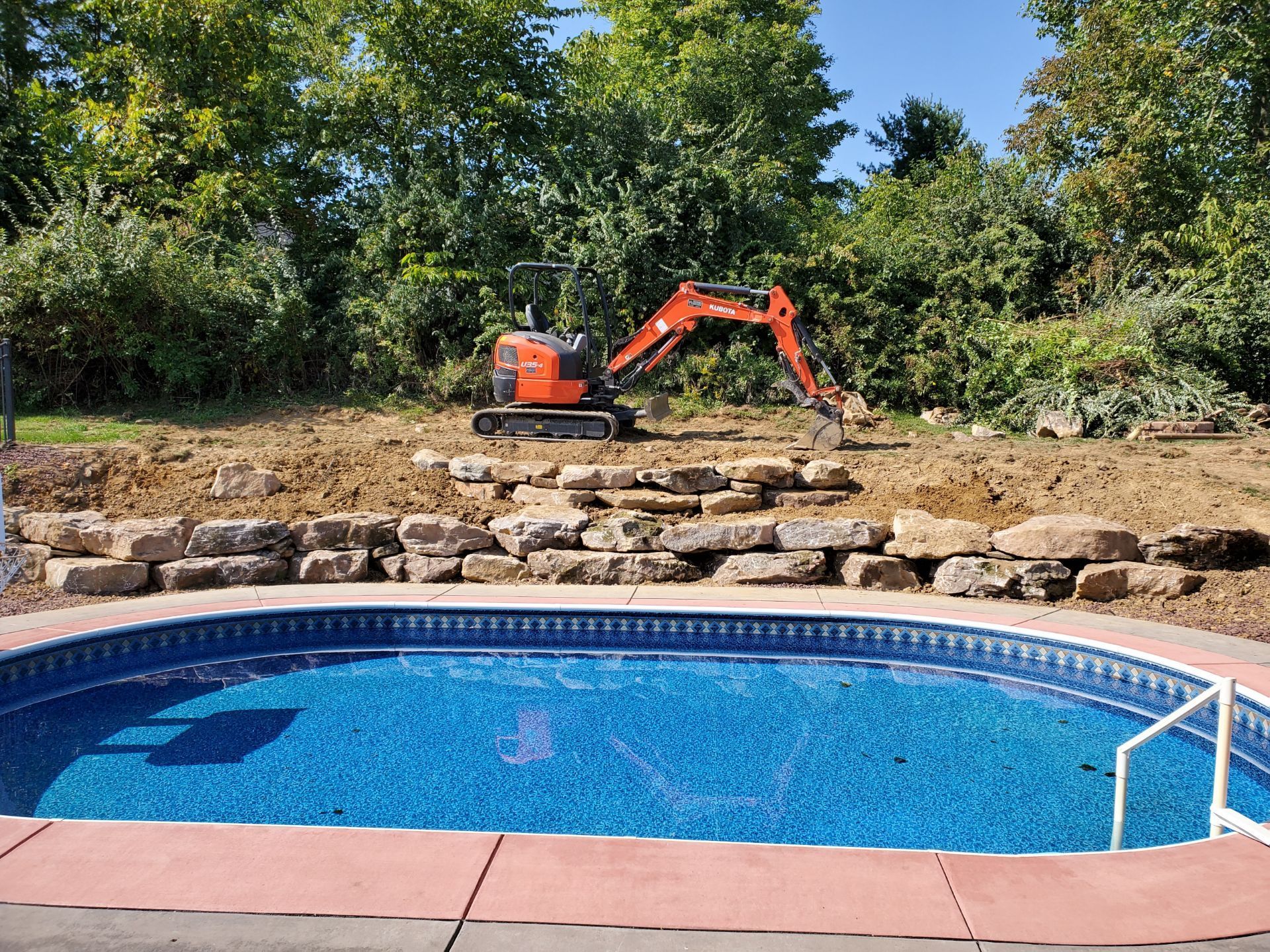 An excavator is digging in the dirt next to a swimming pool.