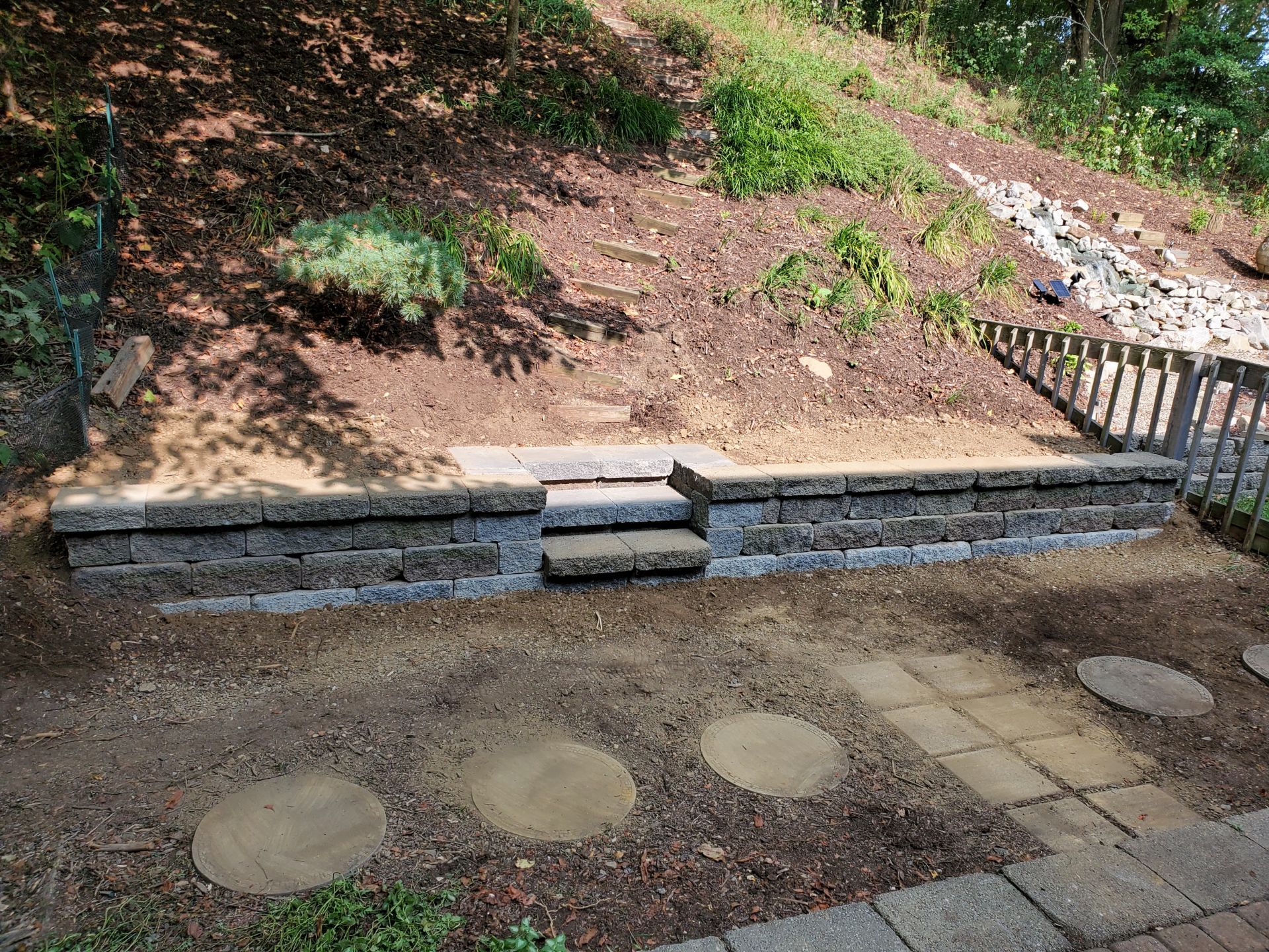 A stone wall with steps leading up to it in a backyard.