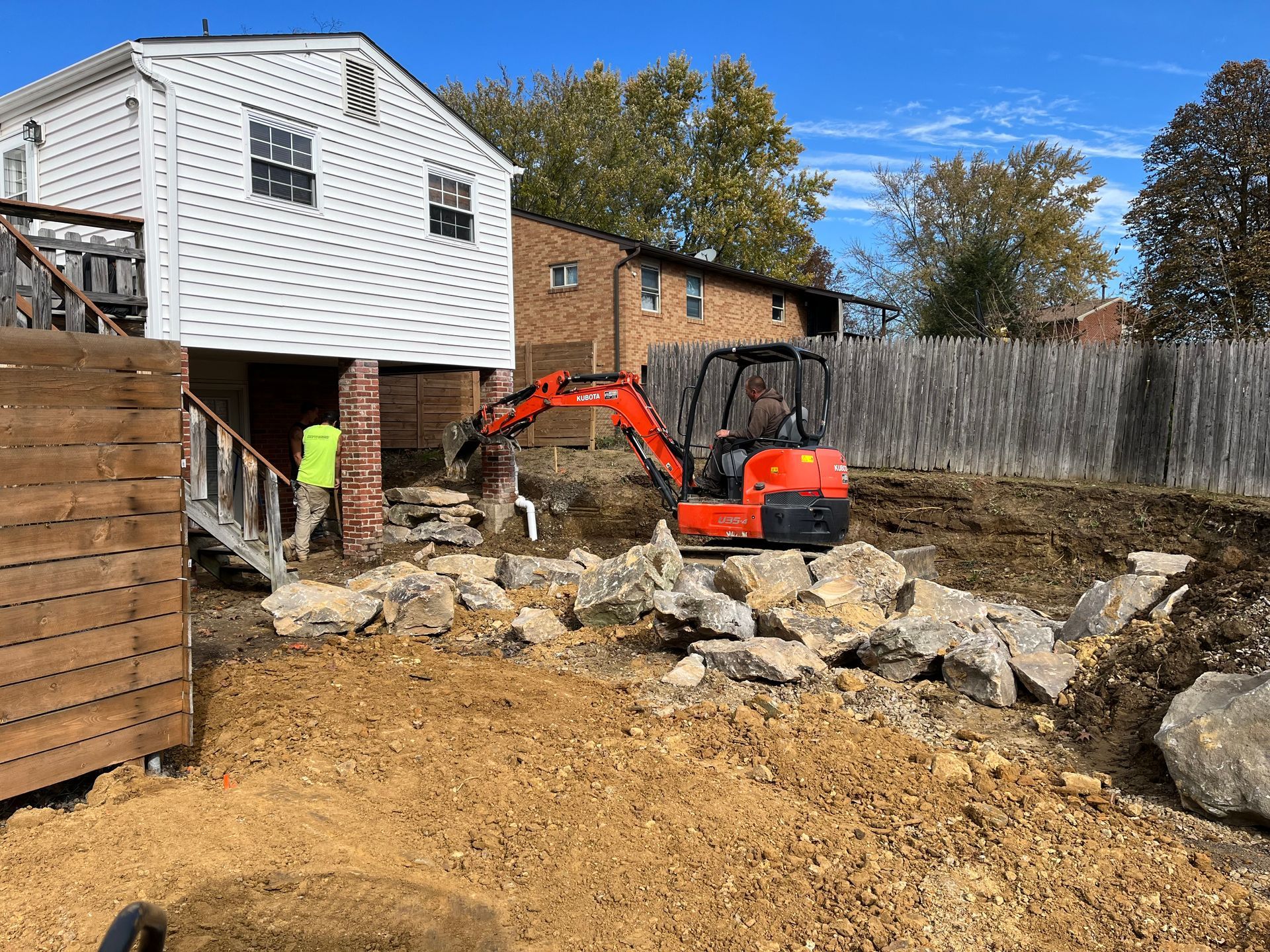 A red excavator is digging a hole in the dirt in front of a house.