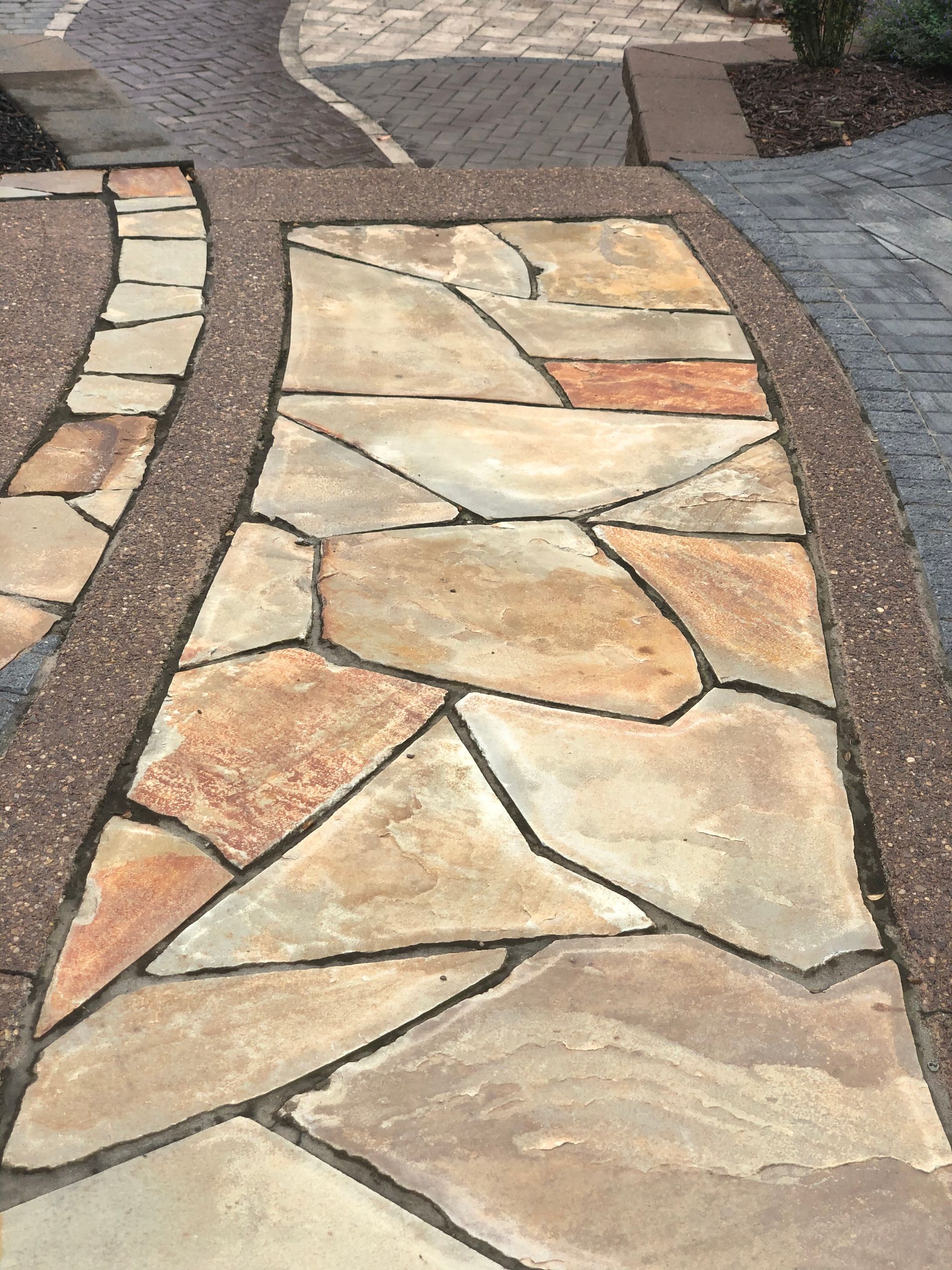 A stone walkway with a brick border and a brick walkway in the background.
