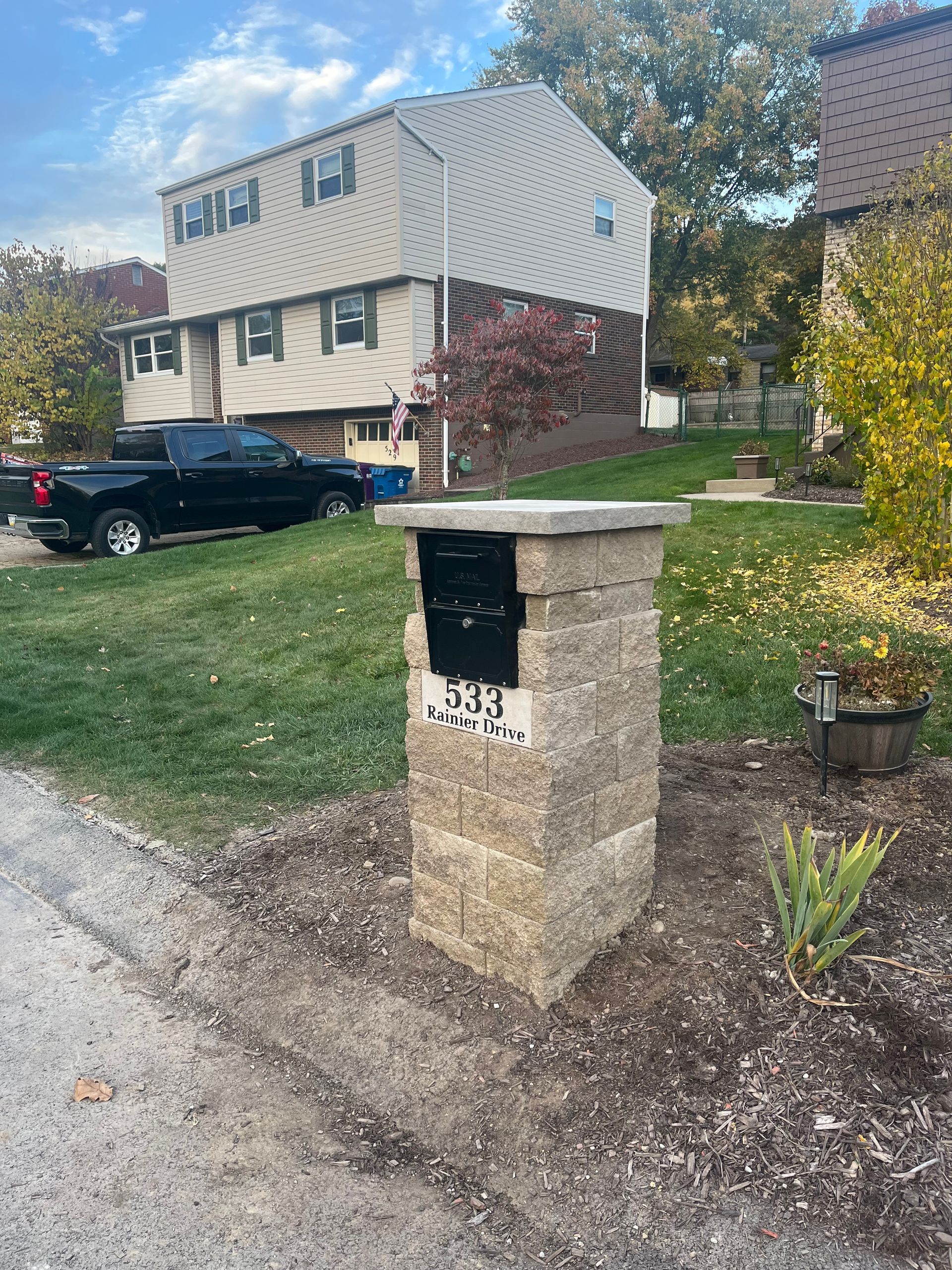 A mailbox is sitting on a brick post in front of a house.