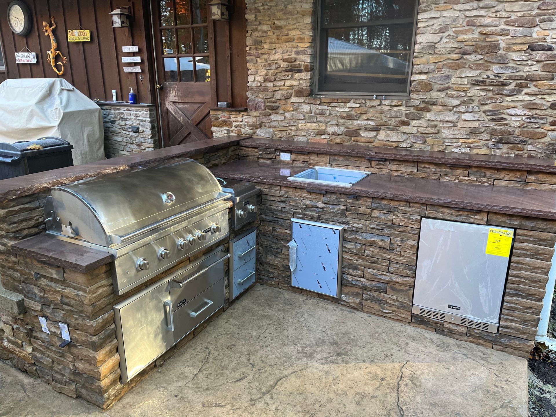 An outdoor kitchen with a grill, sink, and brick wall.