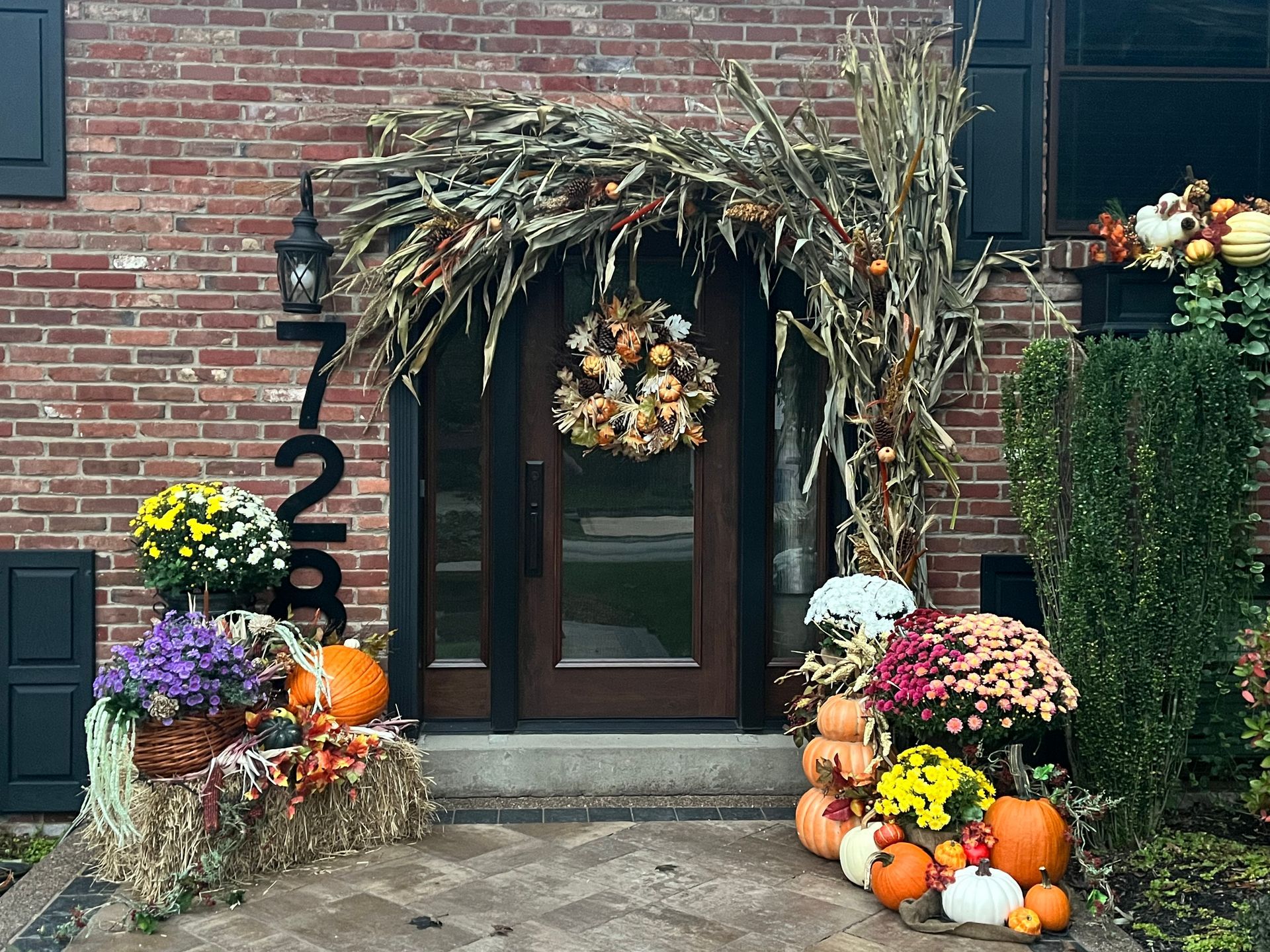 The front door of a brick house decorated for fall with pumpkins and flowers.