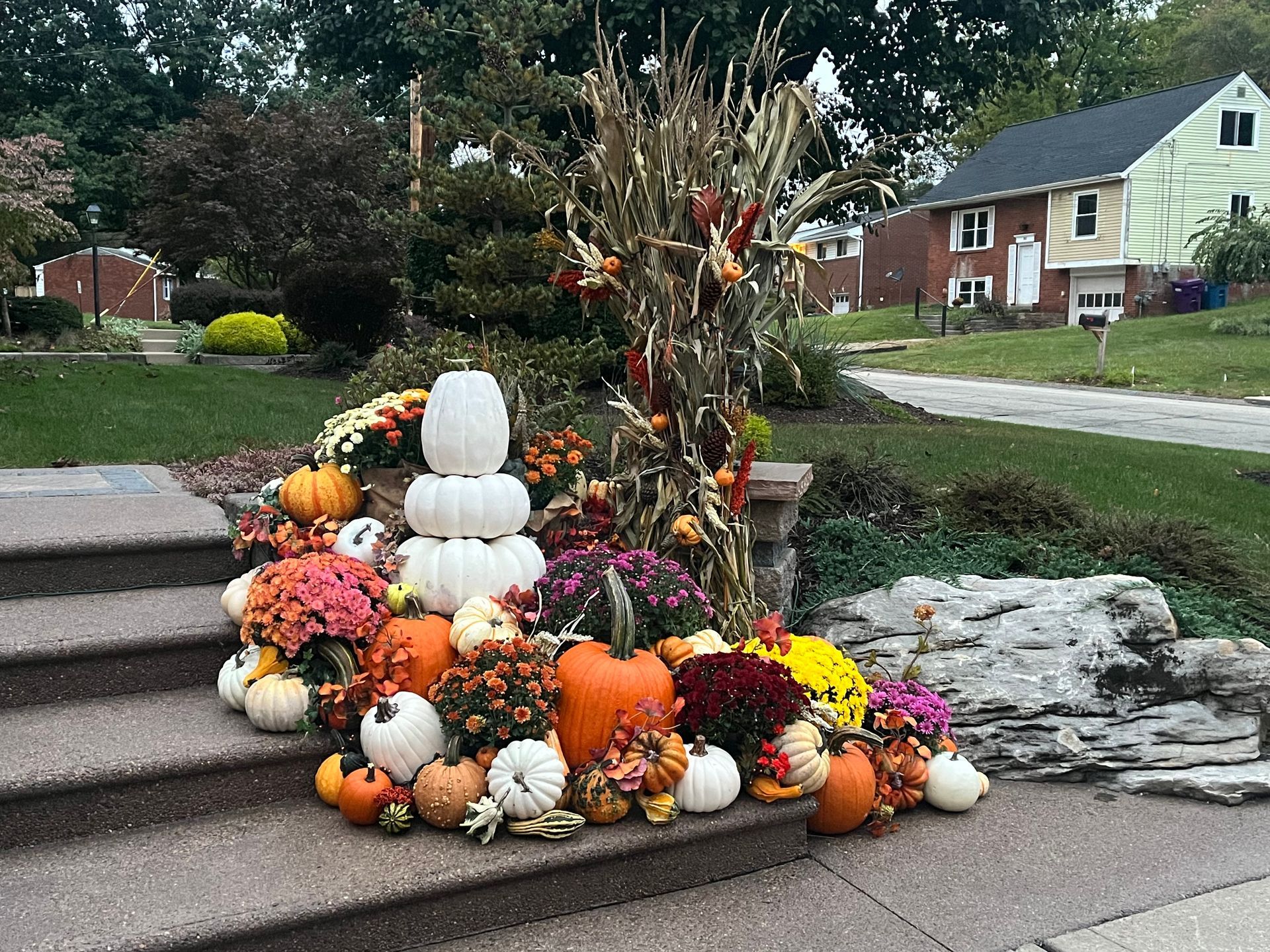 A pile of pumpkins and flowers on the steps of a house.