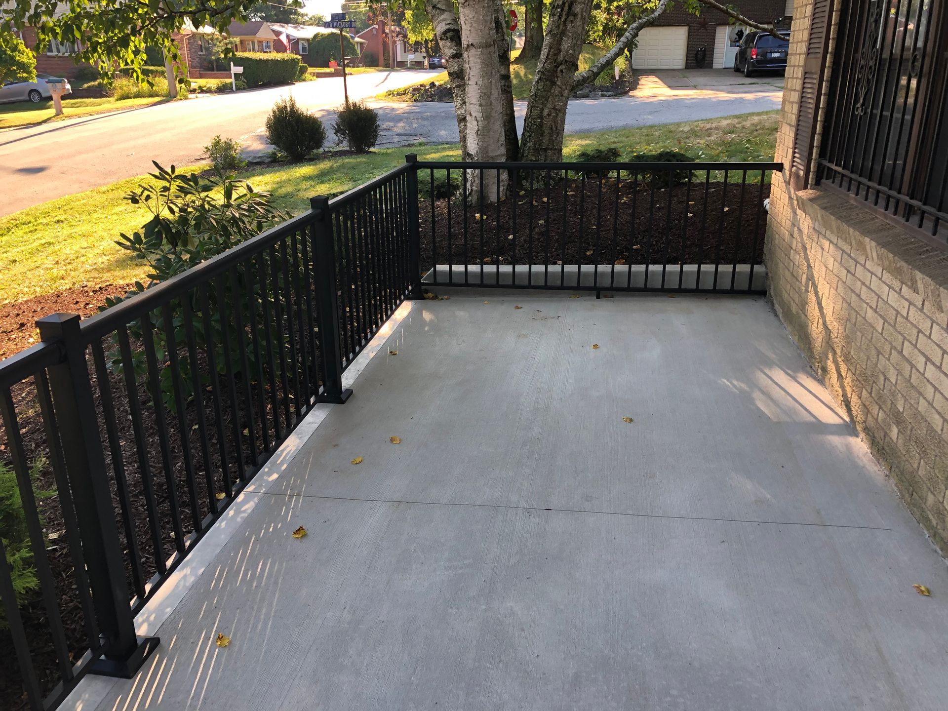 A concrete porch with a black railing and a brick house in the background.