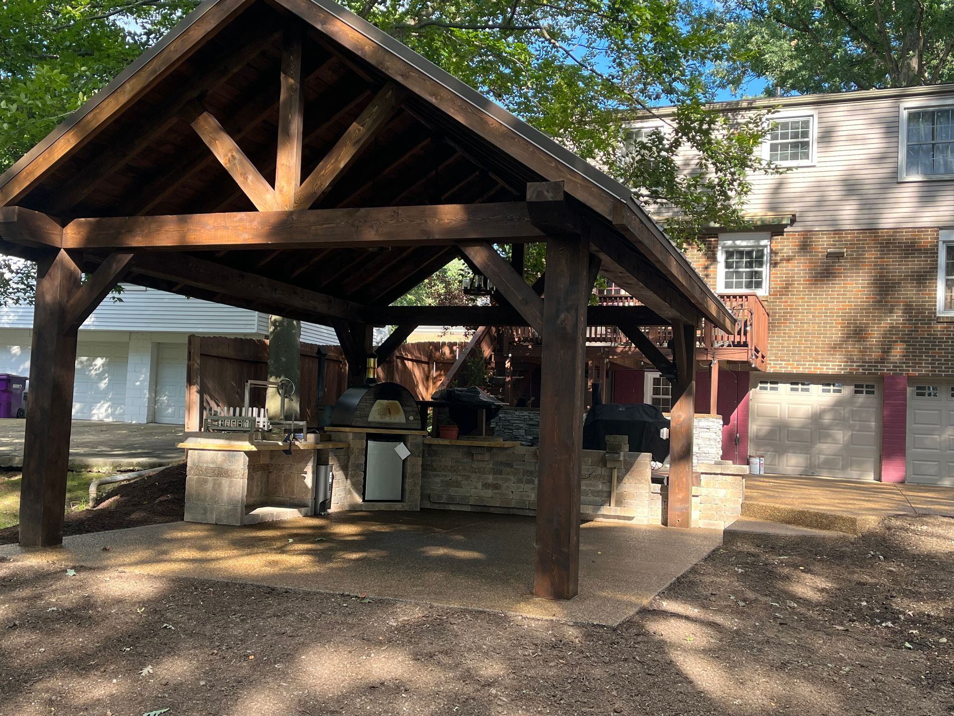 A wooden pavilion with a kitchen in the backyard of a house.