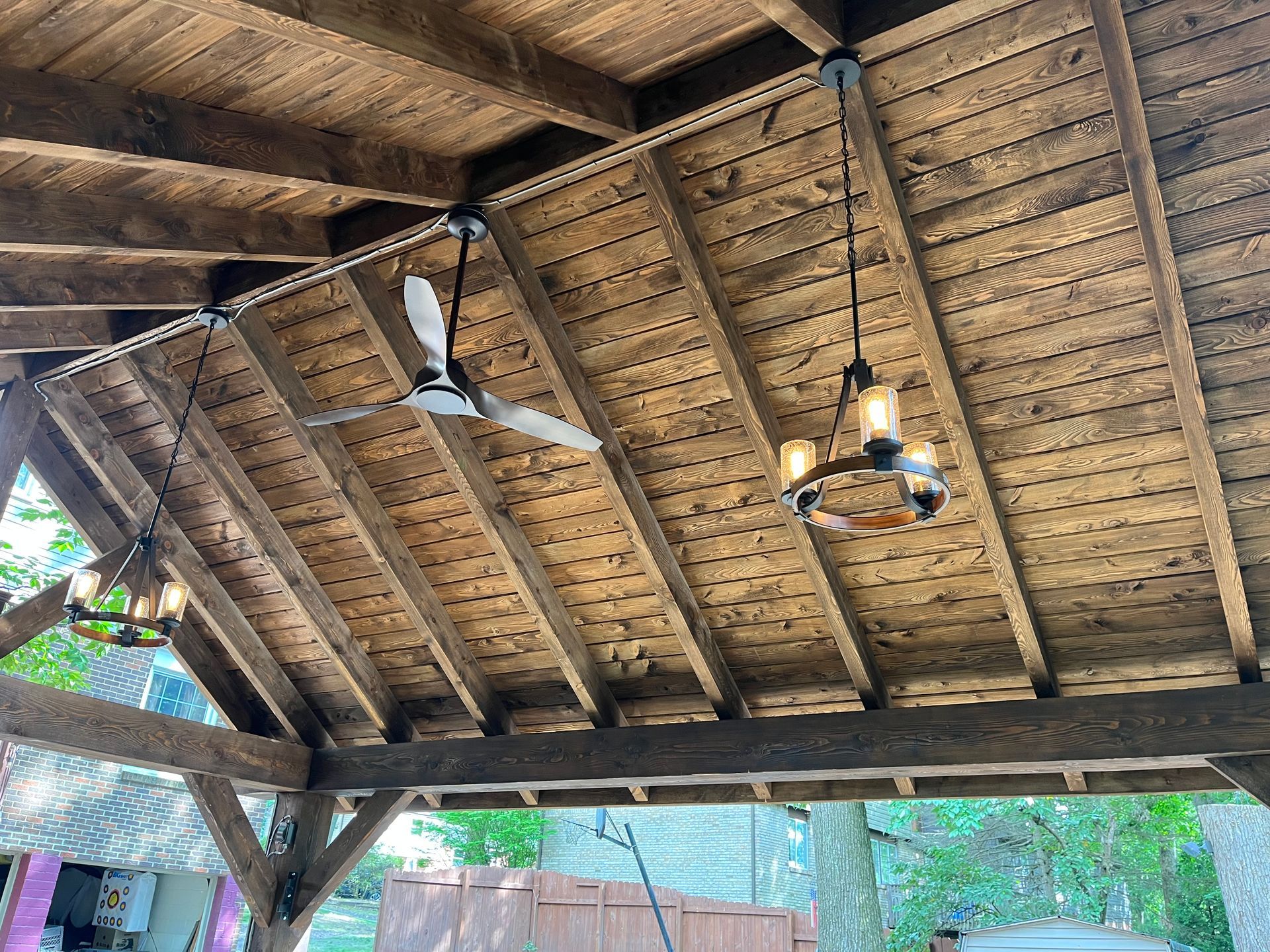 A wooden ceiling with a ceiling fan and a chandelier hanging from it.