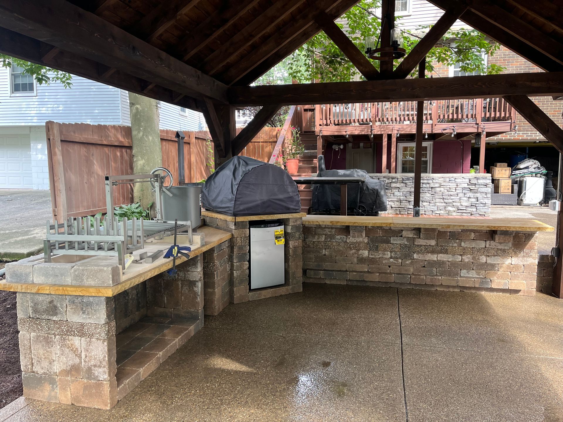 A large outdoor kitchen with a brick counter top and a wooden roof.