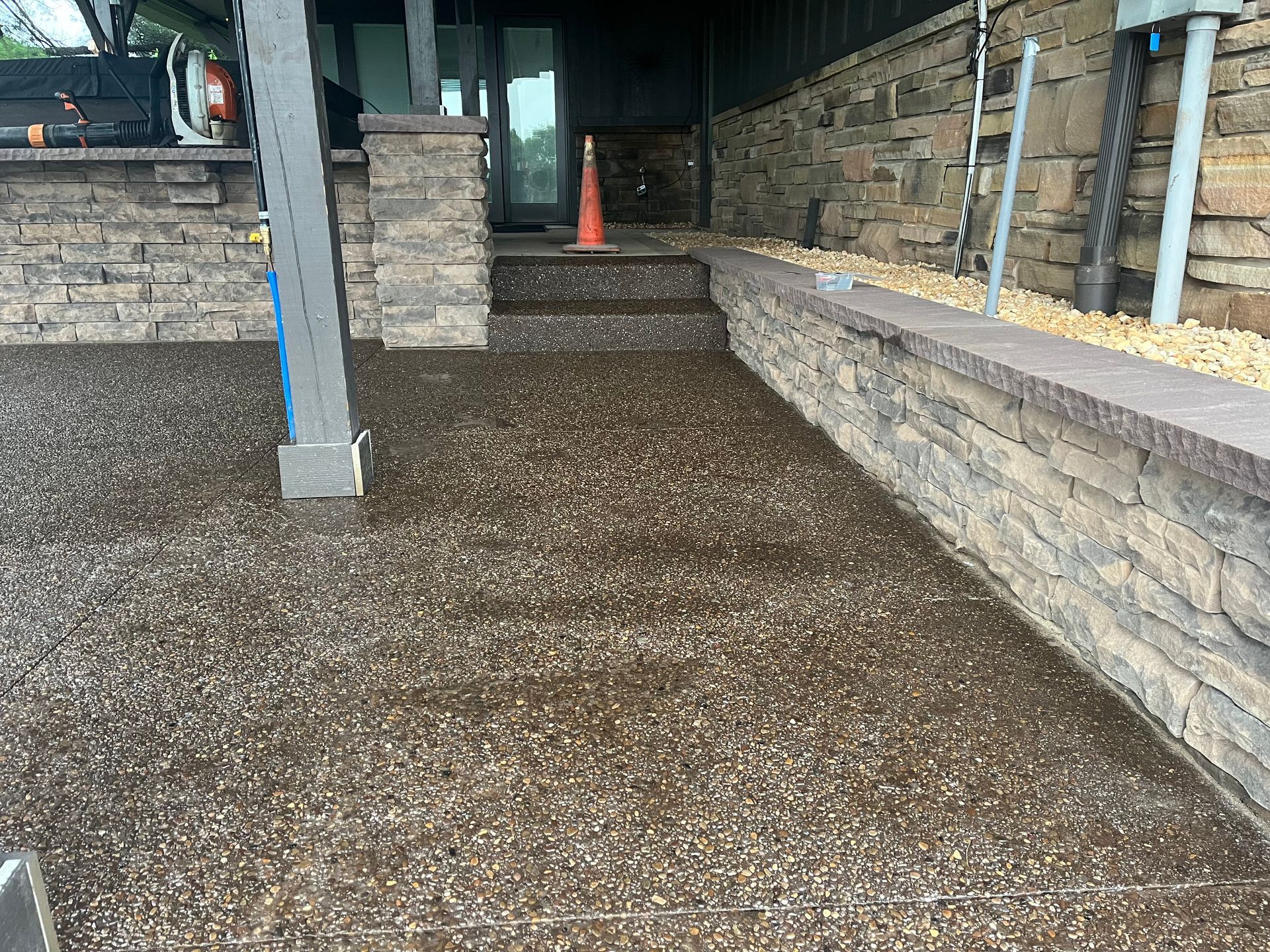 A concrete driveway with a stone wall and a cone in the middle.