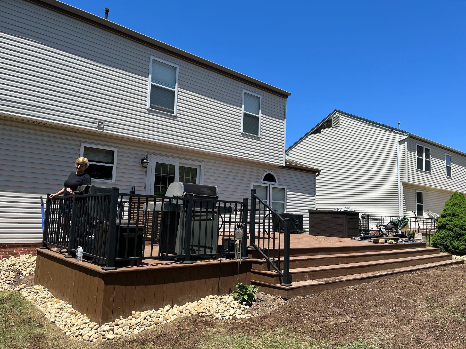 A woman is sitting on a deck in front of a house.