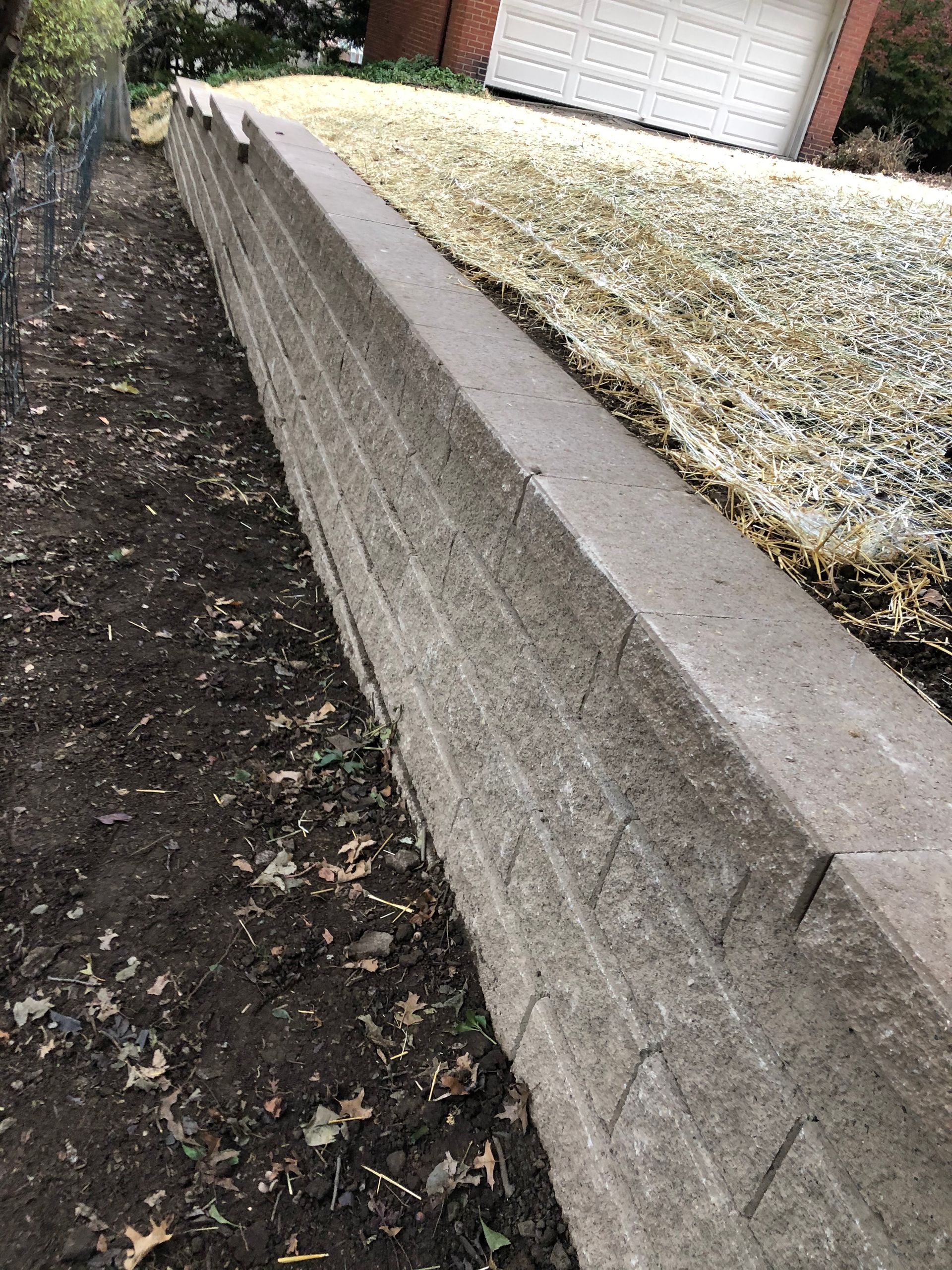 A concrete wall is sitting next to a gravel driveway in front of a house.