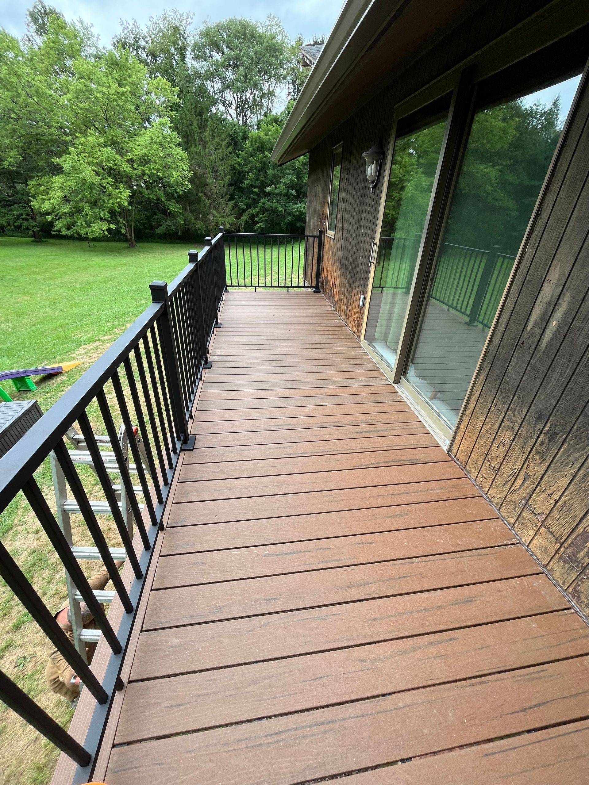 A wooden deck with a black railing on the side of a house.