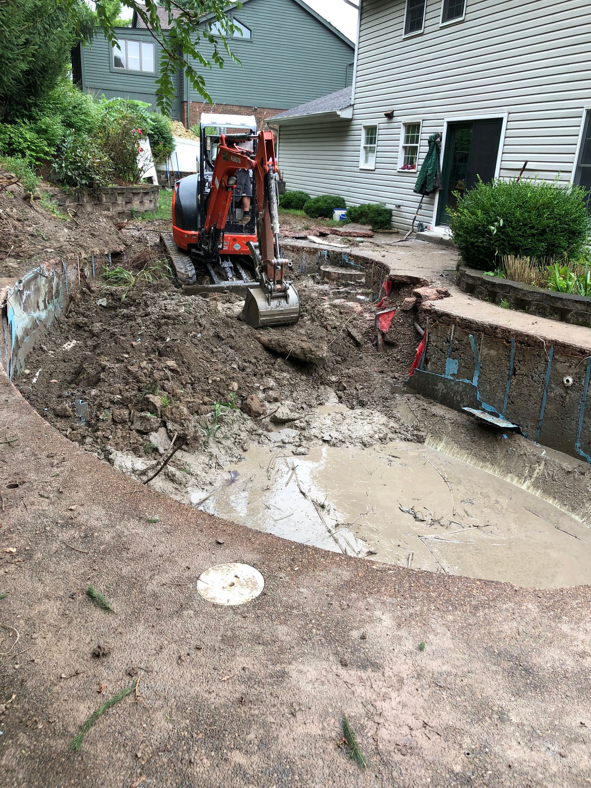 An excavator is digging a hole in the dirt in front of a house.