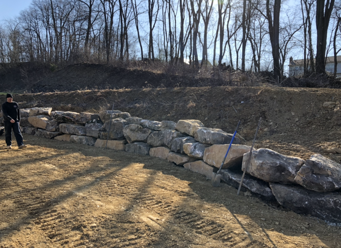 A person is standing on a dirt road next to a river in the woods.