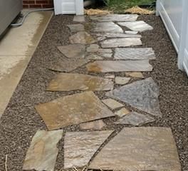 A flagstone walkway set in small, dark gravel leading between a brick wall and a white fence.