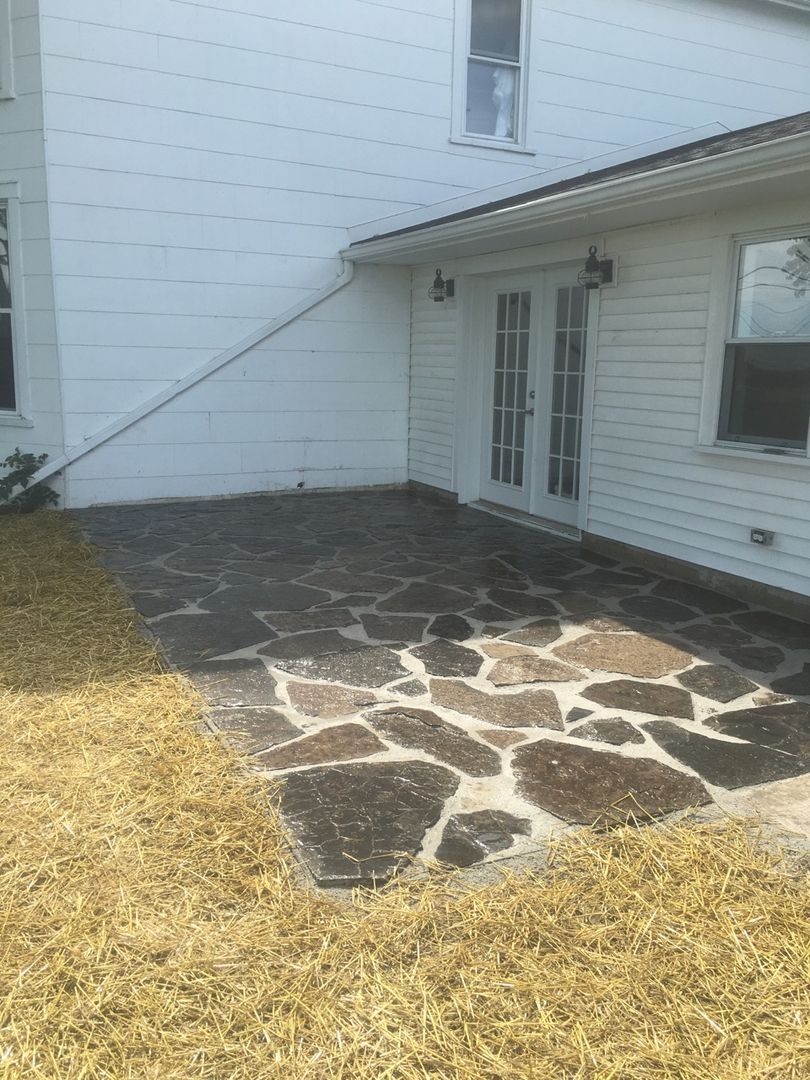 A flagstone patio sits in front of a white house with French doors and an area of dried grass in the foreground.