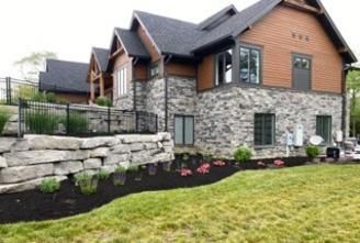 A two-story house with stone masonry on the lower level, wood siding above, and a terraced stone wall in the front yard.