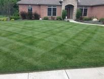 A manicured lawn in front of a brick house with a cross-hatch pattern created by freshly mowed grass.