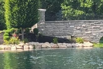 Stone wall with a landscaped garden edge beside a calm pond.