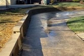 A concrete retaining wall borders a residential driveway that has wet spots from recent rain or cleaning.