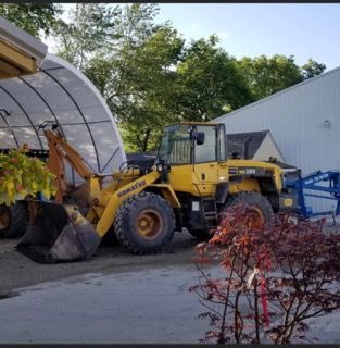 A yellow Komatsu front loader parked outdoors near a white canopy structure and a building.