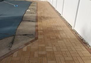 Paver walkway beside a covered pool and white fence in a backyard.