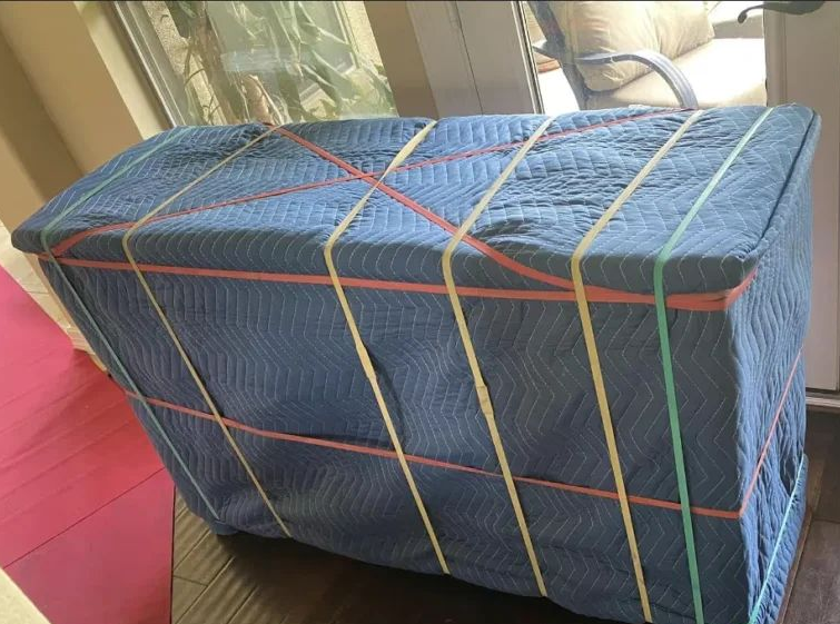 Blue rectangular bale wrapped with colorful straps on a red floor near a window