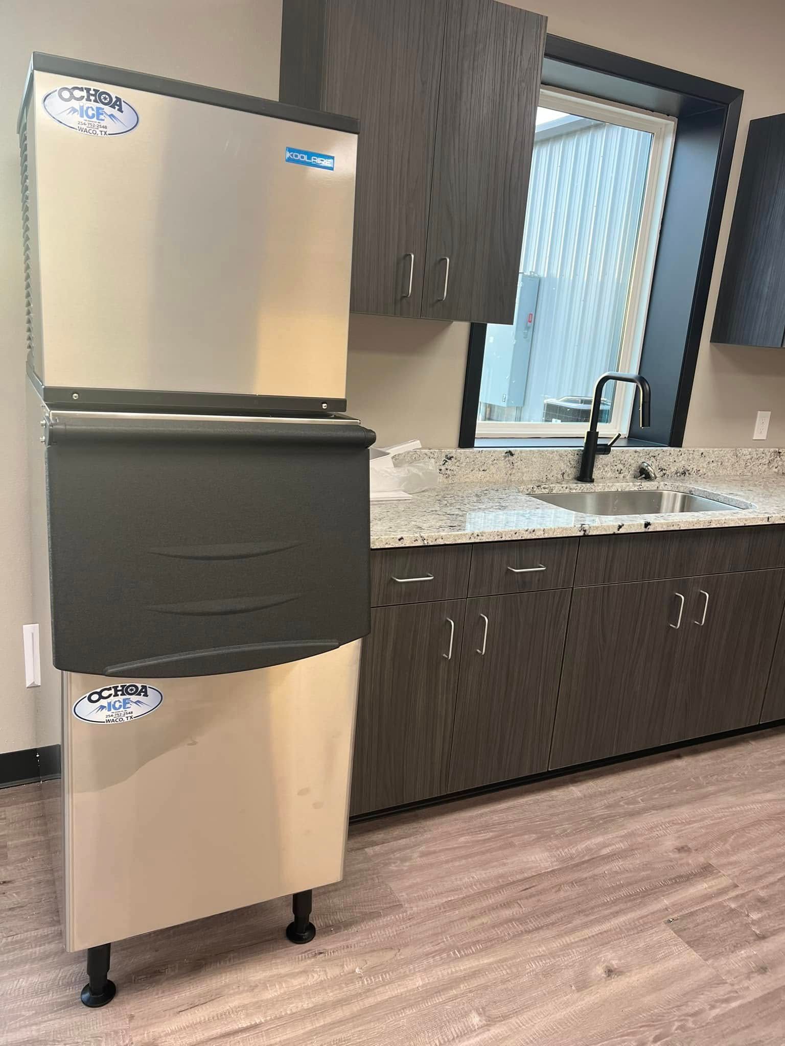 A stainless steel ice maker is sitting in a kitchen next to a sink.