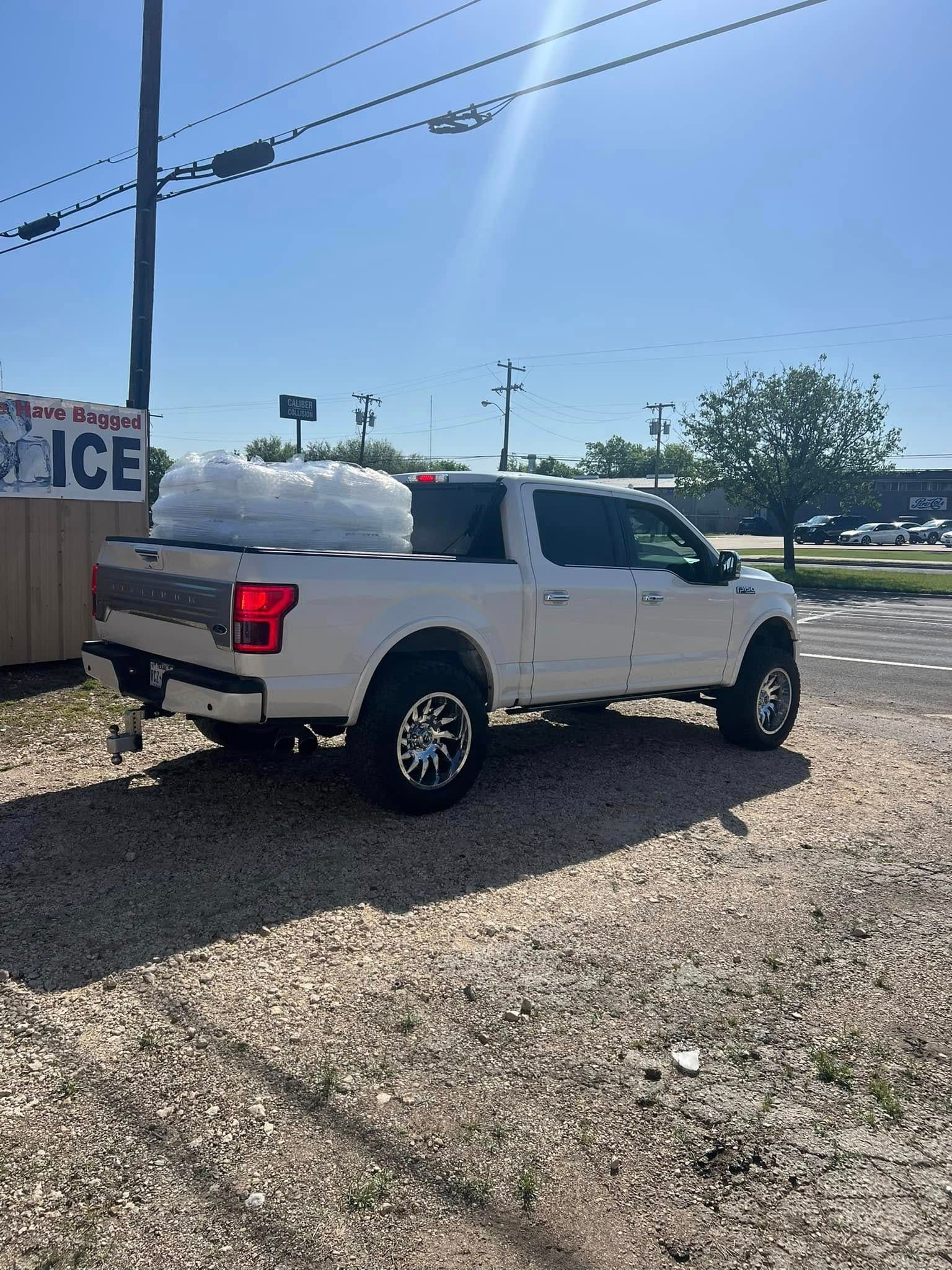 A white truck with ice on the back is parked in a gravel lot.