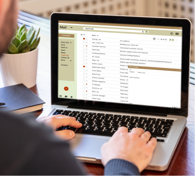 A man is typing on a laptop with an email on the screen