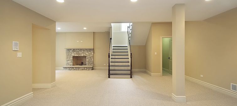 A finished basement with beige walls, a stone fireplace, and a staircase leading upstairs.