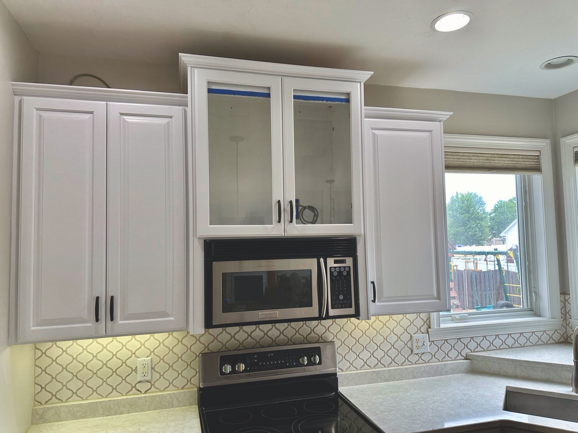 A kitchen with white cabinets , a stove and a microwave.