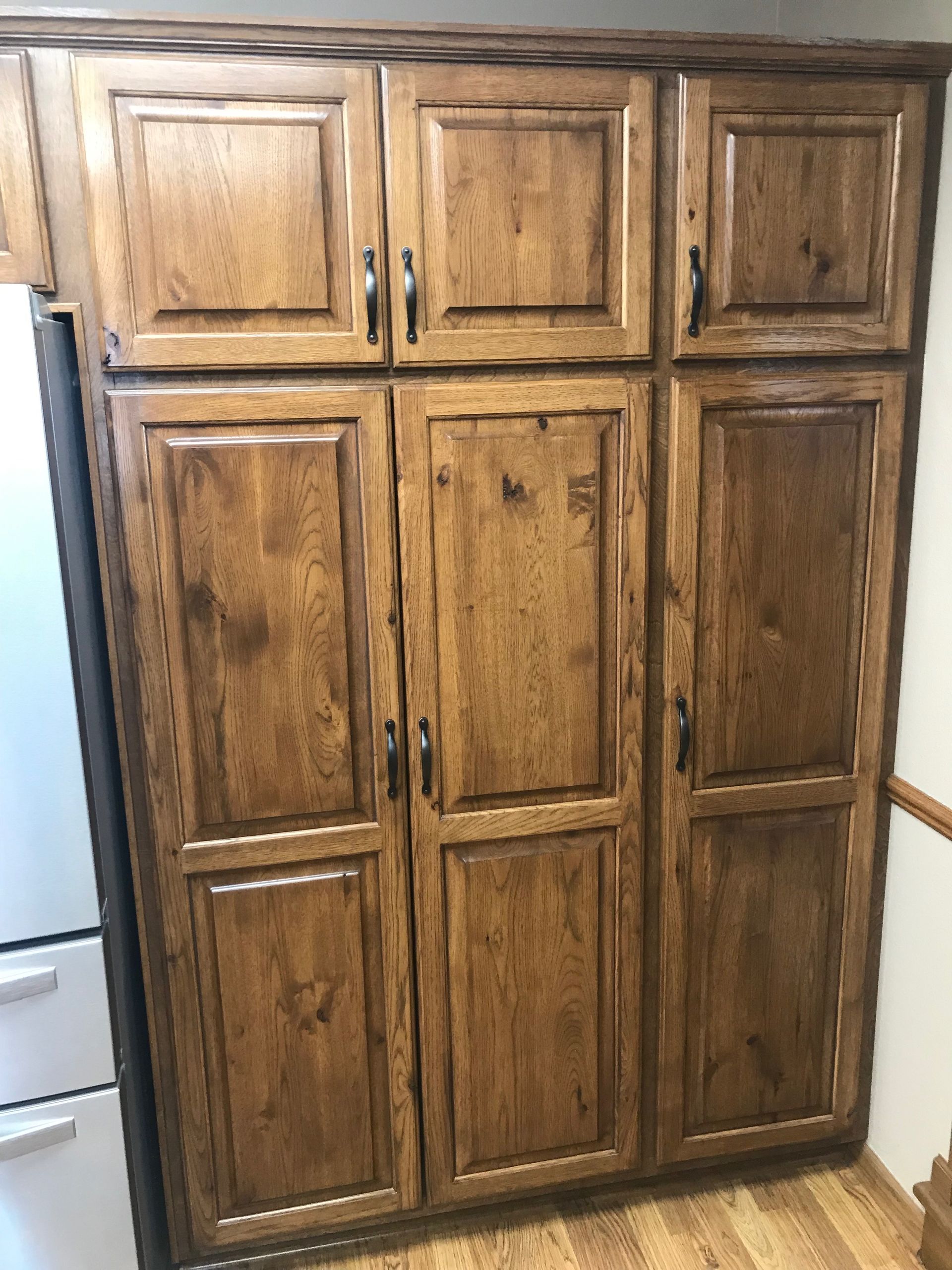 A large wooden cabinet in a kitchen next to a refrigerator.