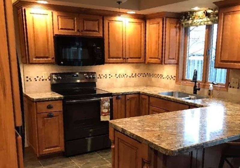 A kitchen with wooden cabinets , granite counter tops , a stove , microwave and sink.