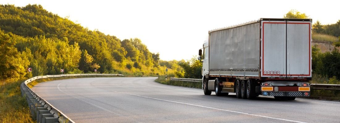 Truck driving on a winding road beside a forested hillside at sunset