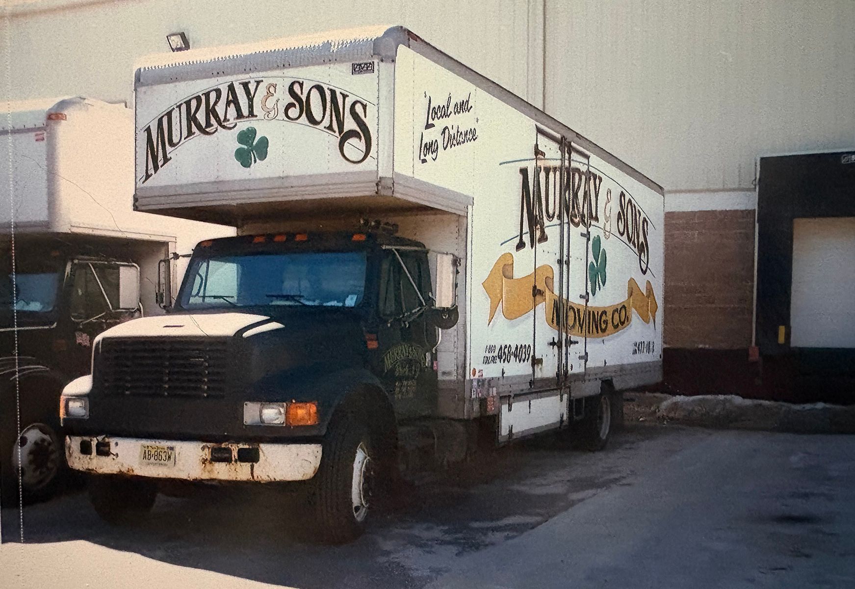 Murray & Sons moving truck parked by a building, black cab with white box trailer.
