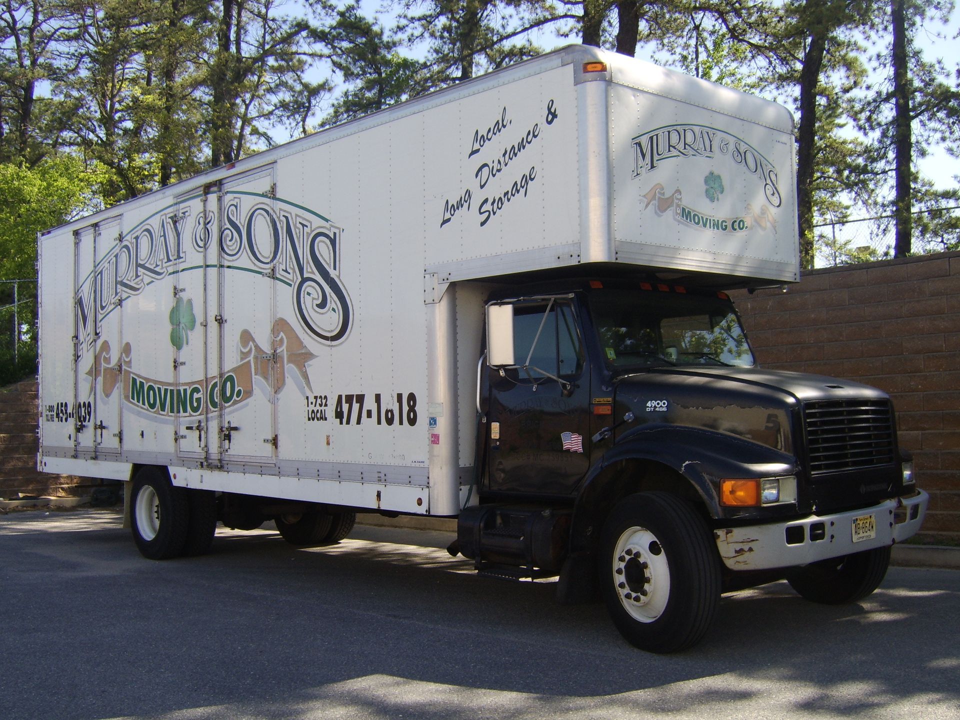 White moving truck with black cab and company logo parked outdoors among trees.