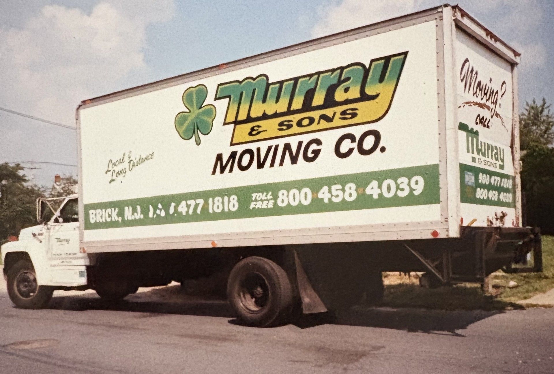 White moving truck with green-and-gold “Murray & Sons Moving Co.” lettering parked on a street