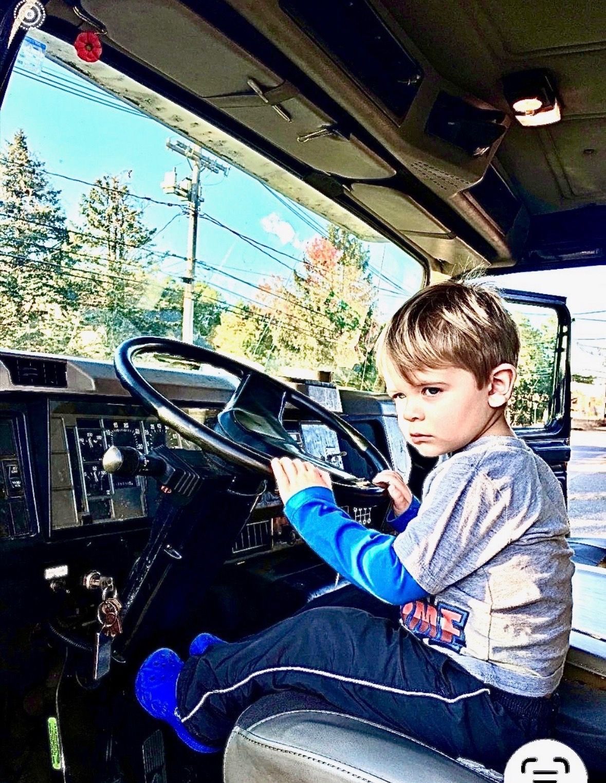 Child sitting in a vehicle driver’s seat, holding the steering wheel and looking at the dashboard.