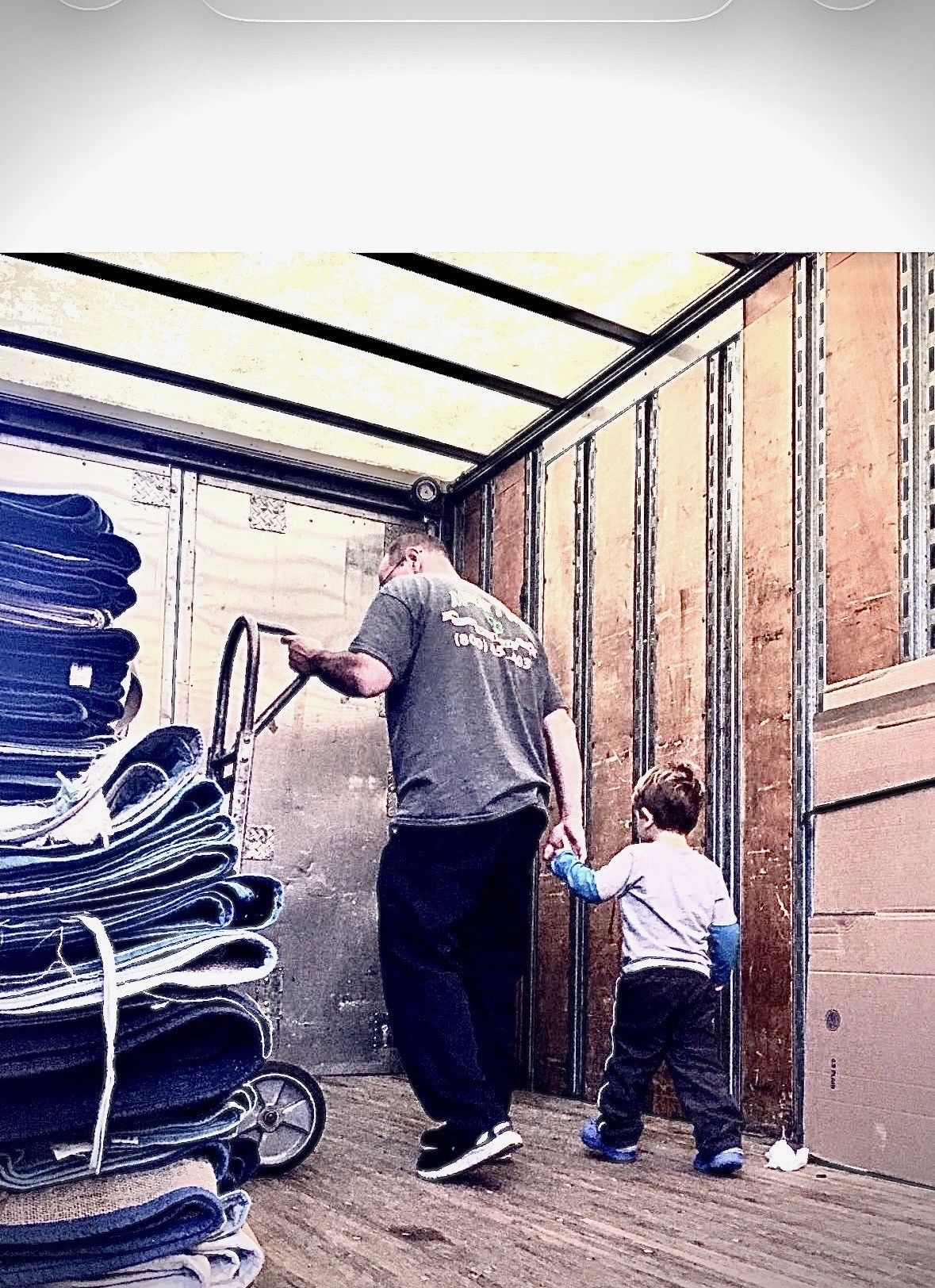 Two people unloading rolled carpets from a truck interior