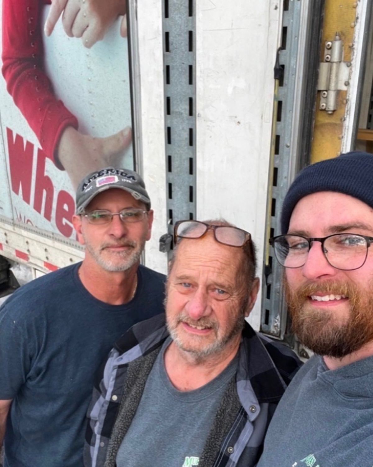 Three men posing beside a truck, smiling at the camera.