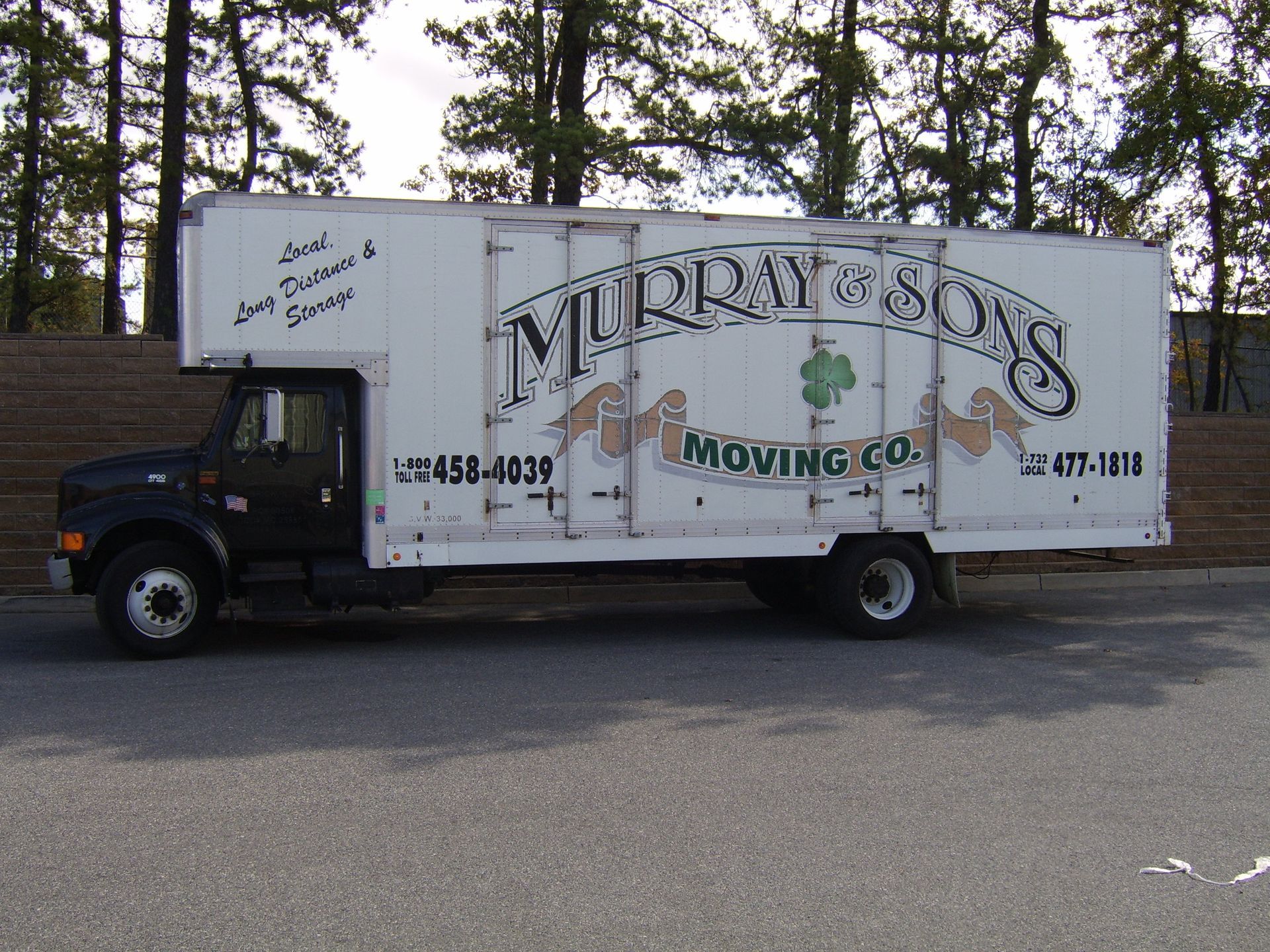 White moving truck with “Murray’s Moving Co.” logo parked outdoors by trees.