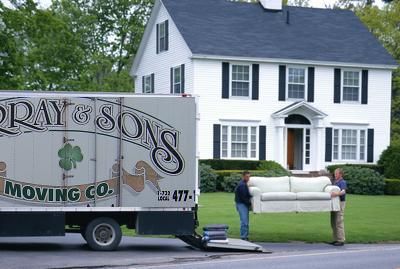 Moving truck beside a white house while movers carry a sofa onto the lawn.