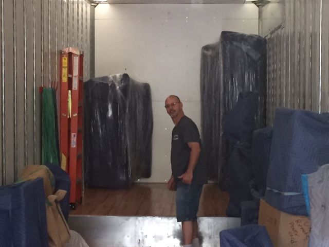 Man standing in a storage unit beside wrapped furniture and stacked items